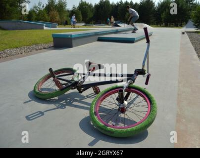 Dobrograd, Region Wladimir, Russland. 29. Juli 2017. BMX Bike liegt auf der Strecke im Skatepark. Teen auf Skateboard führt einen Trick auf dem Hintergrund Stockfoto