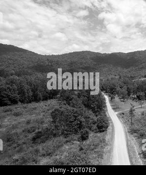 Schwarz-Weiß-Landschaft, einschließlich einer langen Schotterstraße, die durch Buschland zur Bergkette führt Stockfoto