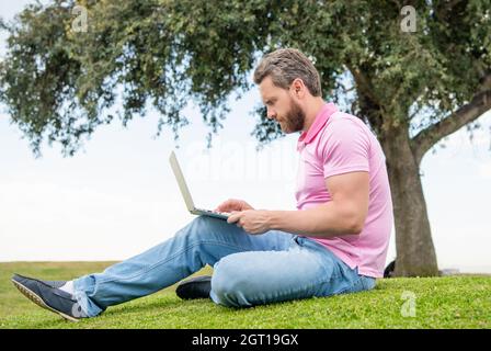 Konzentrierter Geschäftsmann mit Laptop zum Bloggen auf grünem Gras, arbeiten online Stockfoto