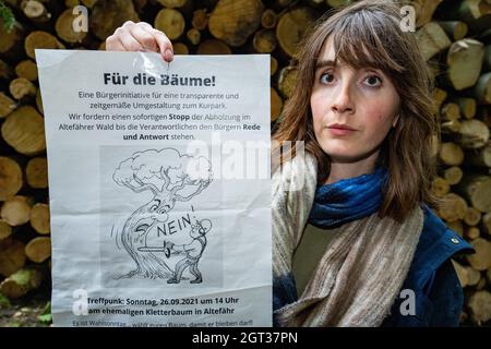 30. September 2021, Mecklenburg-Vorpommern, Schaprode: Franziska Mackels, Bürgerinitiative Kurpark, steht mit einem Plakat vor abgesägten Baumstämmen in Altefähr an der Strandpromenade. Das Fällen von Bäumen auf der Insel Rügen führt in der Gemeinde Altefähr zu Ressentiments. Nach Angaben der Gemeinde soll ein Kurpark aus dem Jahr 1884 mit Blick auf Stralsund restauriert werden. Nach dem Zweiten Weltkrieg wurde der Park in einen Wald verwandelt und wurde seit 30 Jahren seit dem Fall des Kommunismus nicht mehr gepflegt. Die Gemeinde rechnet mit Gesamtkosten von rund einer halben Million Euro Stockfoto