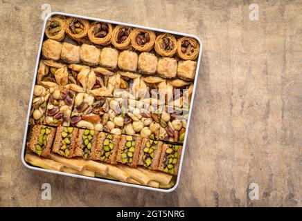 Auswahl an traditionellem türkischen Baklavagebäck in einer Blechdose gegen handgemachtes Papier mit Kopierfläche, ein Dessert ist auch als Perser oder Leber bekannt Stockfoto