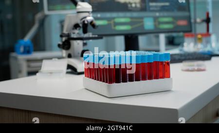 Nahaufnahme von Staubsaugern mit Blut oder roter Flüssigkeit im Labor auf dem Schreibtisch. Tablett mit Glastestflaschen für dna, vorbereitet für die Flüssigkeitsanalyse. Medizinische Geräte und Mikroskop für die Entwicklung Stockfoto