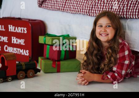 Lächelnd lockiges kleines Mädchen posiert mit Weihnachtsgeschenken. Frohe Weihnachten und ein glückliches neues Jahr Konzept. Stockfoto