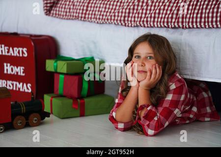 Lächelnd lockiges kleines Mädchen posiert mit Weihnachtsgeschenken. Frohe Weihnachten und ein glückliches neues Jahr Konzept. Stockfoto