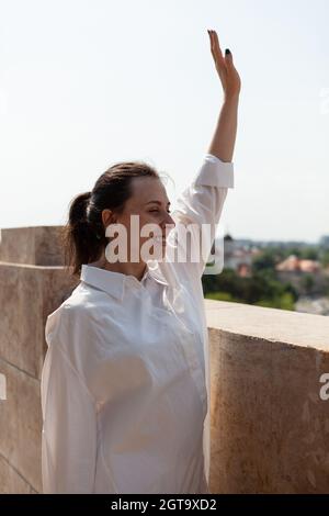 Kaukasische Frau begrüßt Menschen, während sie auf der Turmterrasse steht und den Panoramablick auf die Metropole genießt. Landschaft mit städtischem Wolkenkratzer-Dach und Luftaufnahme vom Aussichtspunkt Stockfoto