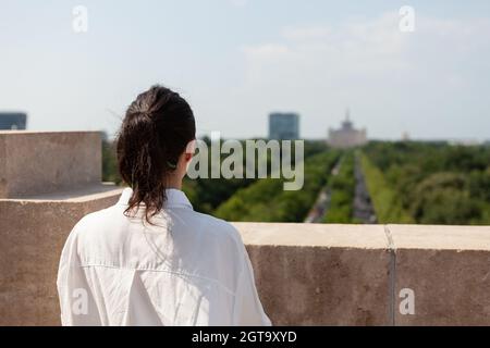 Frau toursit auf dem Dach des Gebäudes und genießt während des Sommerurlaubes den Panoramablick auf die Metropole. Landschaft mit städtischen Gebäuden vom Beobachtungspunkt Stockfoto