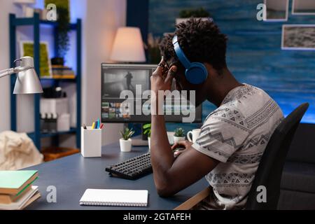 afroamerikanischer Videomaker, der Filmmaterial retuschieren kann, indem er Software für die Nachbearbeitung verwendet, die an visuellen Effekten für Multimedia-Projekte arbeitet. Junger Videofilmer, der am Schreibtisch sitzt und einen Film ansieht Stockfoto