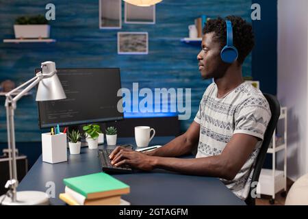afroamerikanischer IT-Mitarbeiter mit Headset, das von zu Hause aus bei der Gestaltung von Websites mit Programmiertechnologien am Computer arbeitet. Programmierer Mann Codierung digitaler Business-Server. Cyber-Sicherheit Stockfoto