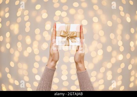 Frau mit einem weißen Geschenkkarton mit einer goldenen Schleife Auf einem hellen Feiertagslicht Hintergrund Stockfoto