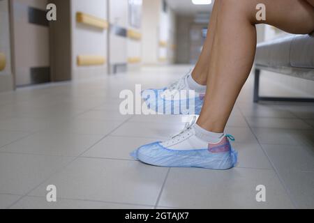 Frauenbeine in Turnschuhen mit Schuhüberzügen im Krankenhausflur Stockfoto