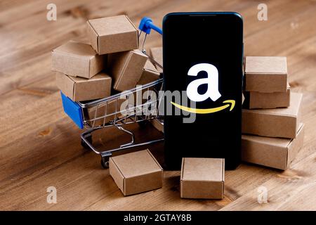 Smartphone mit Amazon-Logo auf dem Bildschirm, Warenkorb und Paketen. Stockfoto