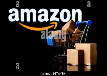 Warenkorb mit Paketen auf schwarzem Hintergrund mit Amazon-Logo. Stockfoto