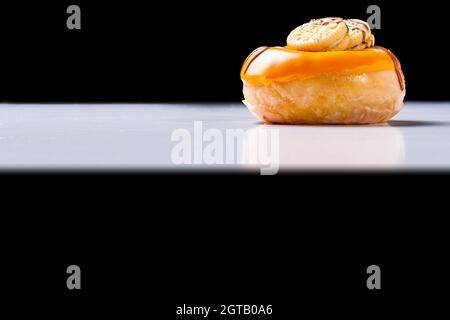 Foto eines mit Schokolade und Keksen bemalten cremefarbenen Donuts auf einem weißen Tisch und schwarzem Hintergrund.das Foto wurde im horizontalen Format A aufgenommen Stockfoto