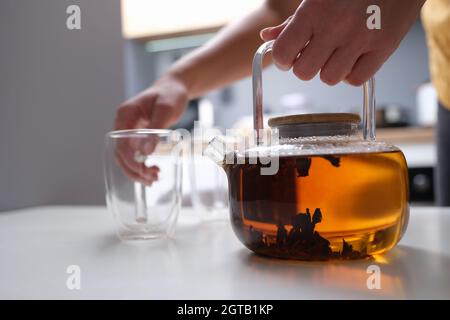 Frau Hand hält transparente Teekannen mit Tee und Glas Tasse Nahaufnahme Stockfoto