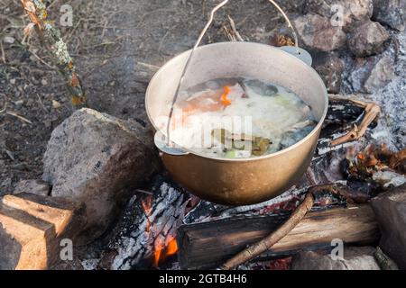 Touristensuppe mit Gemüse kocht in einem Kessel. Vorbereitung auf ein offenes Feuer, Camping-Mahlzeit Stockfoto