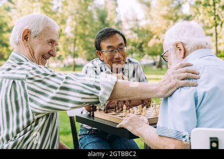 Gruppe älterer Freunde, die im Park ein Schachspiel spielen. Lifestyle-Konzepte über die Altersgruppe und das dritte Alter Stockfoto