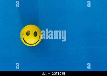 Anthropomorphe Smiley-Gesichtsausdrücke eines Squeeze Ball oder Stress Ball isoliert auf blauem Hintergrund. Tabellenansicht von oben. Nahaufnahme. Happy Smile Hintergrund Stockfoto