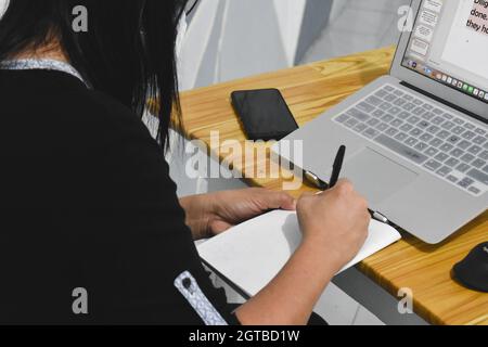 Frau, die auf Papier gegen einen Schreibtisch schrieb Stockfoto
