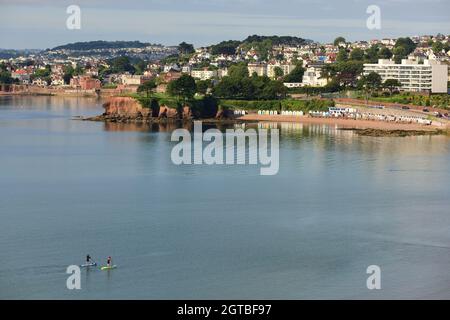 Stand-up-Paddlebarder in Tor Bay, mit Blick auf Corbyn's Head und Livermead von der Torquay-Küste aus. Stockfoto