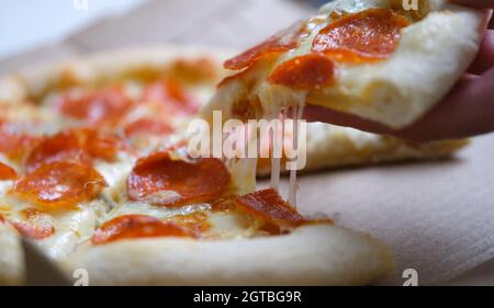 Frau hält ein Stück leckere heiße Pizza über der Schachtel in Nahaufnahme Stockfoto