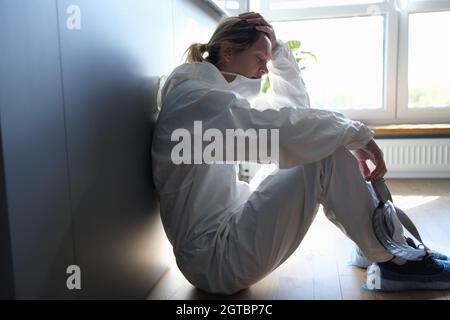 Müde Ärztin im medizinischen Schutzanzug und Maske in den Händen nach der Arbeit in der Klinik Stockfoto