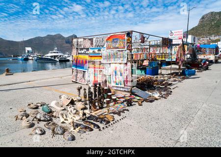 Afrikanische Straßenmarktstände und Händler, die Kuriosen, traditionelle Kunst und Kunsthandwerk sowie Souvenirs im Hafen von Hout Bay verkaufen Stockfoto