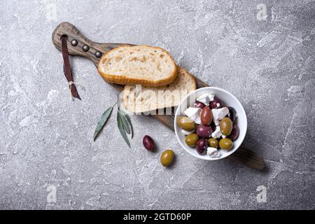 Draufsicht auf leckere Oliven mischen sich mit Feta-Käse und Brotscheiben auf grauem Beton Hintergrund Stockfoto