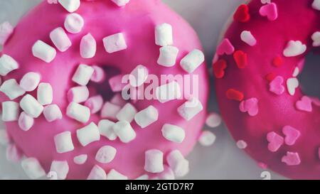 Zwei süße, köstliche rosa Donuts mit Marschmalchen und roten Herzen streuen. Ein schönes Geschenk zum Valentinstag. Essen und Romantik. Stockfoto