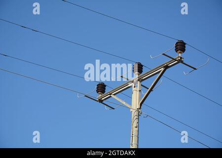 Nahaufnahme des oberen Teils eines Stromverteilungspylons und der Stromleitungen unter blauem Himmel Stockfoto