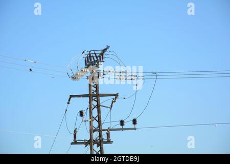 Nahaufnahme des oberen Teils eines Stromverteilungspylons und der Stromleitungen unter blauem Himmel Stockfoto