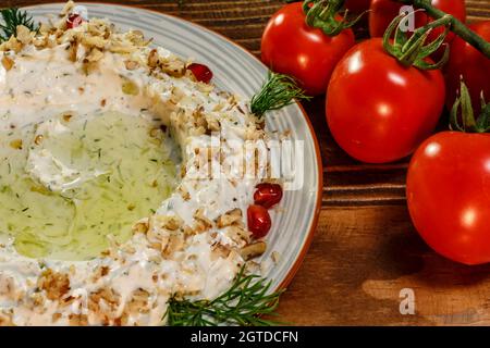 Nahaufnahme von cremigem Salat mit Nüssen, Knoblauch, Gurken und Gemüse, verziert mit Kirschtomaten Stockfoto