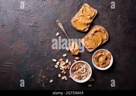 Süsse Erdnusspaste oder Butter mit Honig auf Brot für leckeres Frühstück auf dunklem Betongrund Stockfoto