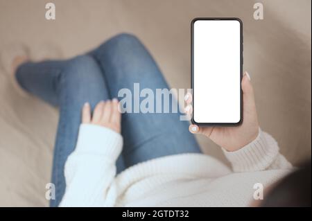 Modell des Mobiltelefons, das von einer Frau im Wohnzimmer gehalten wird. Frau liest Textnachricht auf dem Mobiltelefon mit weißem leeren Bildschirm für Ihre Textnachricht oder Stockfoto