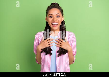 Foto von süß beeindruckt dunkle Haut Frau gekleidet gestreiften Hemd Arme Brust öffnen Mund lächelnd isoliert grüne Farbe Hintergrund Stockfoto