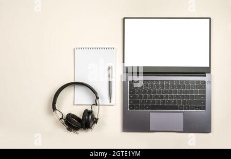 Draufsicht auf Laptop leerer Bildschirm leerer Notizblock und Kopfhörer auf weißem Tischhintergrund mit Text- und Kopierbereich. Mockup Bild von modernen weißen ho Stockfoto
