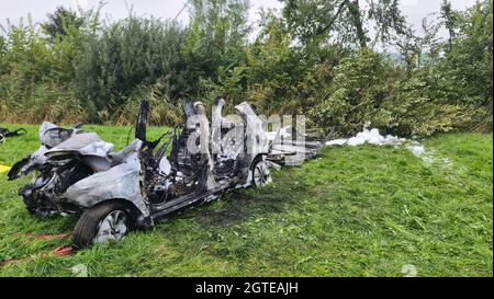 Brunsbuttel, Deutschland. Oktober 2021. 02. Oktober 2021, Schleswig-Holstein, Brunsbüttel: Das ausgebrannte Wrack eines Autos steht am Straßenrand. Bei dem Autounfall in Brunsbüttel im Kreis Dithmarschen wurden drei junge Menschen zu Tode verbrannt. Sie waren im Auto gefangen, als sie in Flammen aufbrachen. Die Einsatzkräfte konnten sie aufgrund der Hitze nicht befreien, so die Feuerwehr. Foto: Karsten Schröder/Westküsten-News /dpa Quelle: dpa picture Alliance/Alamy Live News Stockfoto