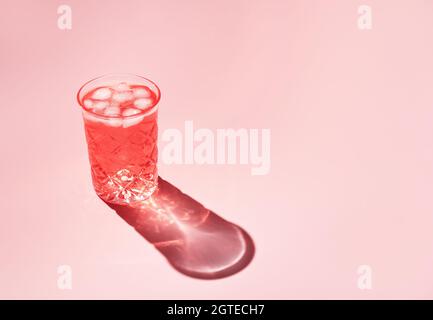 Schönes Kristallglas wirft langen Schatten vom Sonnenlicht auf rosa Hintergrund. Minimale kreative Komposition mit Kopierplatz. Sommergetränke-Konzept. Stockfoto