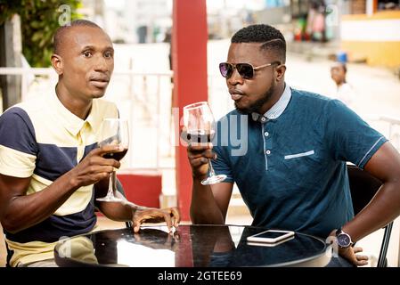 Zwei junge Brüder, die einen Geburtstag feiern, halten jeweils ein Glas Rotwein und lächeln dabei Stockfoto
