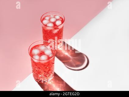 Zwei wunderschöne Kristallgläser werfen lange Schatten vom Sonnenlicht auf weißen und rosa Hintergrund. Minimale kreative Komposition mit Kopierplatz. Sommergetränke-Konzept. Stockfoto