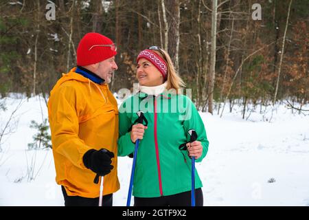 Senior Paar Walking mit nordic Walking Stöcken im verschneiten Winter Wald Stockfoto