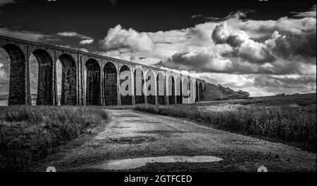 Schwarz-Weiß-Bild des Ribblehead Viadukts Yorkshire UK. Mit offener Straße und Wasserbecken. Klarer Himmel, aber dramatische Wolken. Keine Personen. Stockfoto