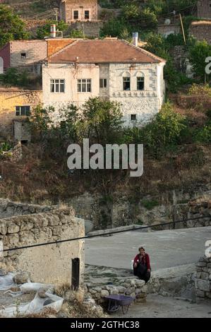 Alltag in einem ländlichen Dorf in der Türkei ein altes weiß getünchtes Haus und eine Frau, die in Zentralanatolien sitzt und wartet Stockfoto