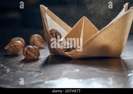 Schnecken in Papierboot auf Metall Restaurant Küchentisch Stockfoto