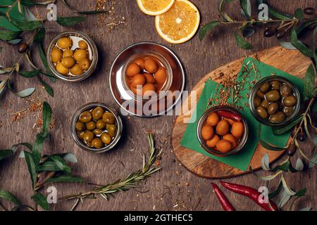 Set aus verschiedenen marinierten Oliven auf Holz Hintergrund in Schalen mit Gewürzen und Olivenblättern dekoriert. Stockfoto