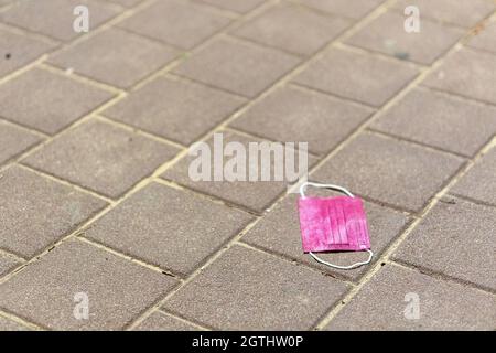 Pink Medical Face Mask zum Schutz vor Coronavirus, das auf einem Parkplatz auf den Boden geworfen wird. Verlassene Coronavirus-Maske in Parki auf den Boden geworfen Stockfoto