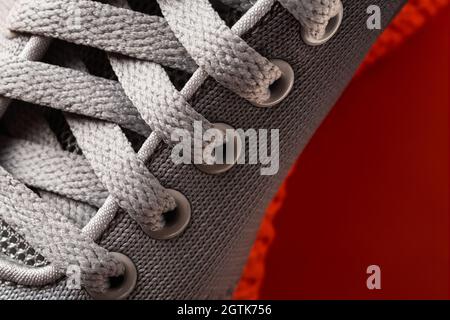 Schnürung von grauen Textil-Sneakers mit oranger Sohle aus nächster Nähe. Neuer Sportschuh mit Schnürung. Elastische Schnürsenkel von modernen Turnschuhen aus Mesh-Material für Fitness. Stockfoto