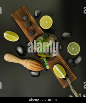 cuba libre, Rum und Cola Cocktail in einem Glas mit Limette und Minze auf schwarzem Hintergrund auf einem Holzbrett Stockfoto