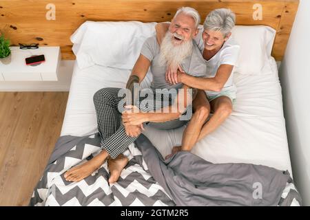 Glückliches Seniorenpaar lächelt zusammen im Bett - Hipster-reife Menschen mit zarten Momenten im Schlafzimmer - älterer Lebensstil und Liebesbeziehung Konzept Stockfoto