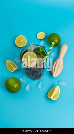 Sommerlicher kühlender Cocktail mit Rum, Eis und reifer Limette, in Keile geschnitten, auf einem klaren blauen Hintergrund Stockfoto