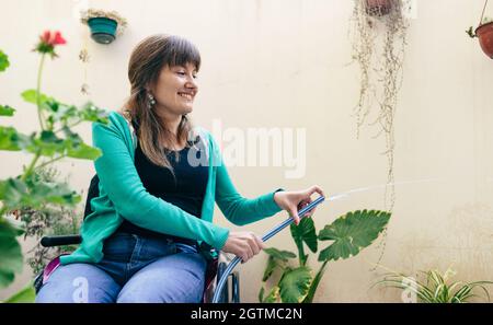 Junge Frau im Rollstuhl Bewässerung Pflanzen Stockfoto